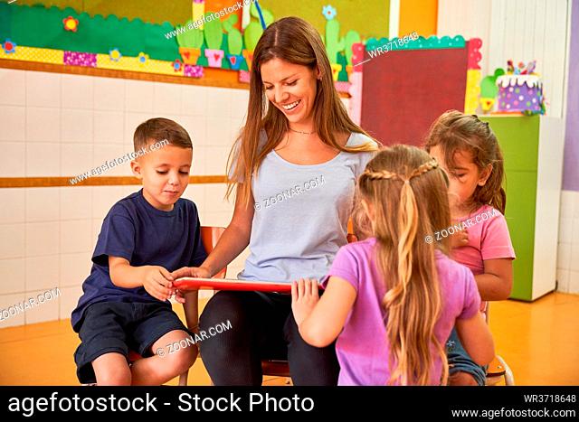 Lächelnde Tagesmutter beim Buch vorlesen für eine Gruppe Kinder im Kindergarten oder Hort
