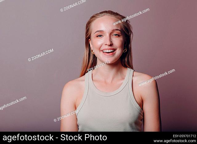 Portrait of young smiling european woman. Beautiful happy blonde girl wears t-shirt and looks at camera. Studio shoot isolated on pink background