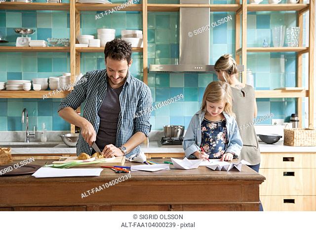 Young daughter drawing ar kitchen counter while parents prepare meal
