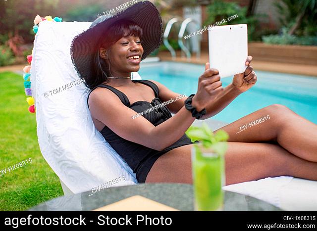 Happy young woman video chatting with digital tablet at poolside