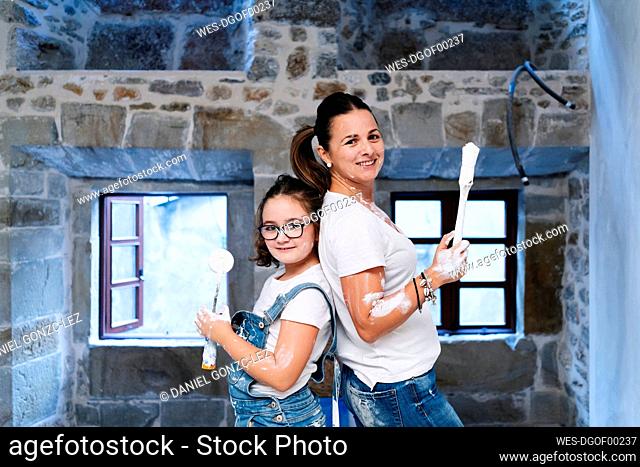 Portrait of mother and daughter posing with paintbrush and paint roller