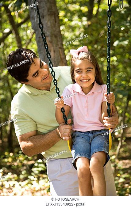 Hispanic father pushing daughter on swing