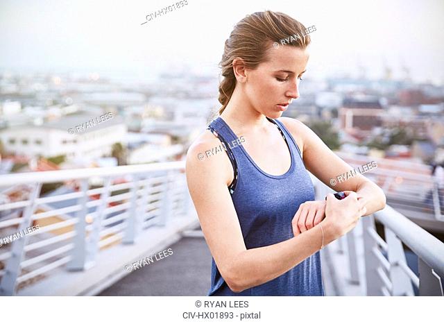 Female runner checking smart watch fitness tracker on urban footbridge