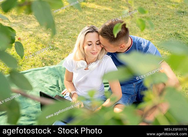 Affectionate young man kissing girlfriend enjoying picnic at park