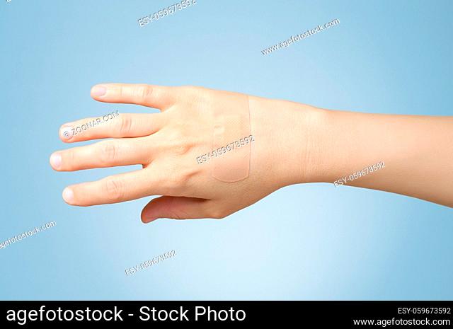 Female hand with adhesive bandage on blue background
