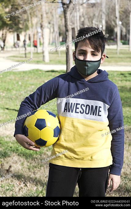 Kid playing football wearing a green mask. Coronavirus protection
