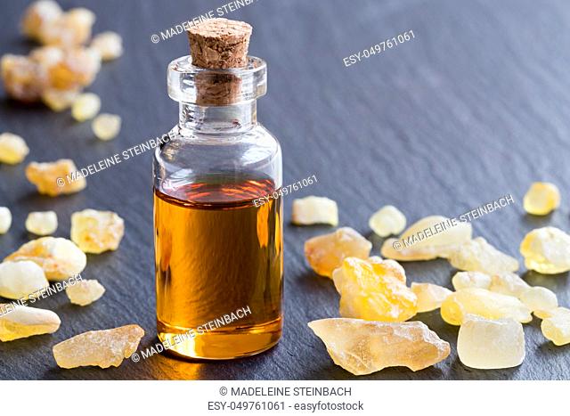 A bottle of frankincense essential oil with frankincense resin on a dark background