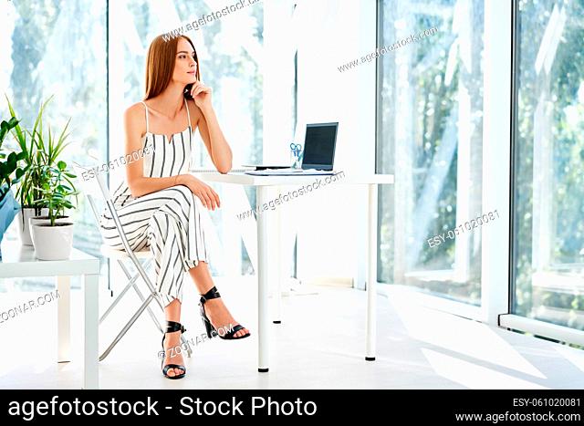 Pretty smiling businesswoman posing in a modern office sitting on her desk. business success concept, people at work