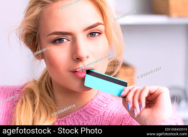 Beautiful woman biting edge of credit card portrait. Pretty blondhaired girl wearing pink putting credit card to her mouth