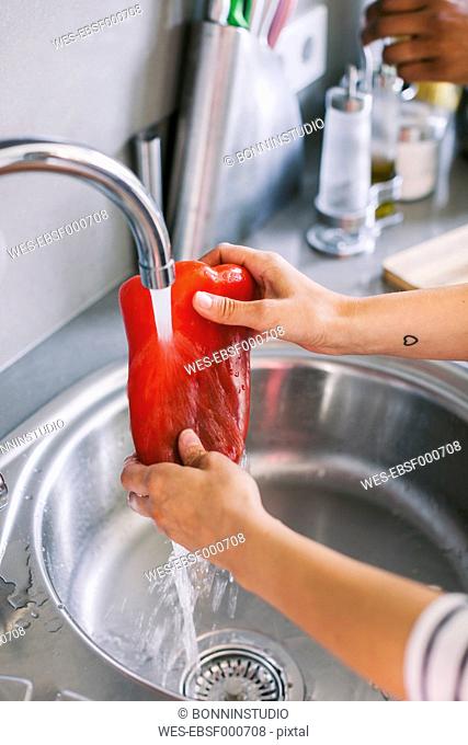 Woman's hands cleaning red bell pepper with flowing water