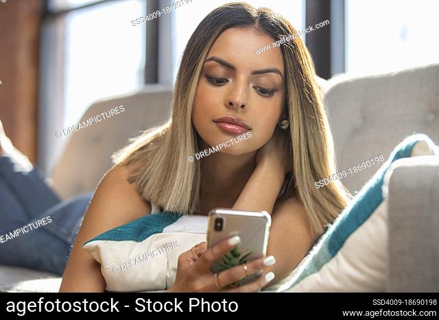 Portrait of Hispanic girl laying on couch mobile phone scrolling