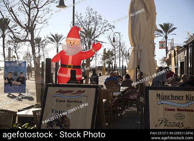 11 December 2023, Spain, Palma: An inflatable Santa Claus stands on the terrace of the ""Munchner Kindl"" restaurant on Arenal beach on a sunny day with a...