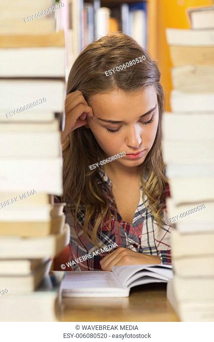 Focused pretty student studying between piles of books