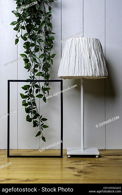 one blank black frame, an ivy and a lamp on the table with a white wood background