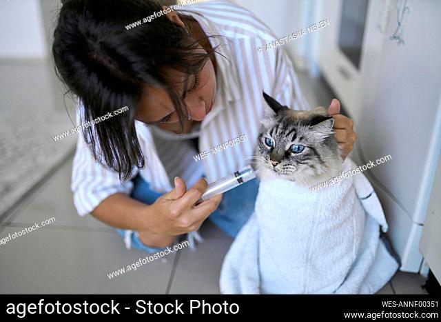 Woman giving medicine to cat at home