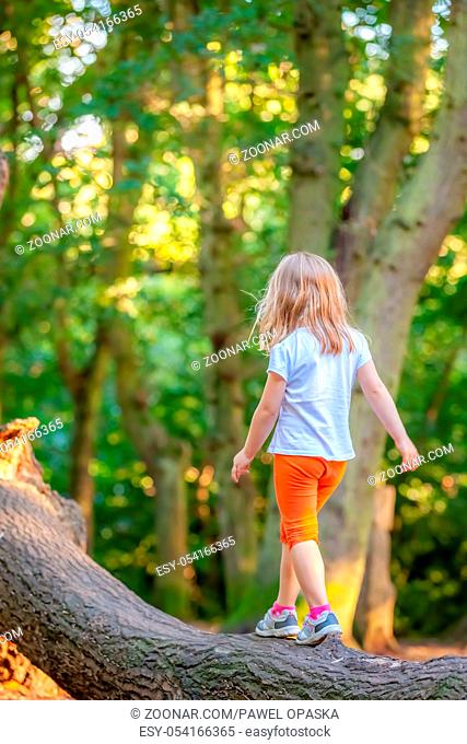 Young Caucasian girl walking on a large tree trunk in a forest