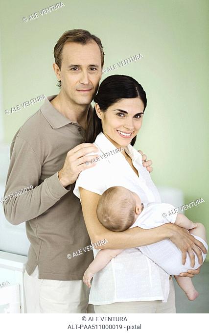 Parents smiling at camera, woman holding baby, portrait