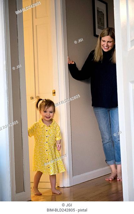 Mother watching Caucasian baby daughter standing in doorway