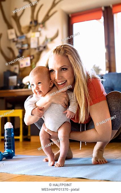 Smiling mother with baby and fitness equipment at home