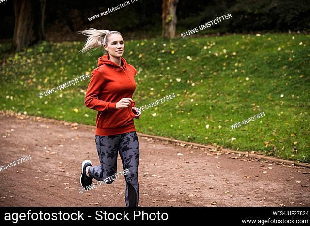 Young athlete wearing hooded shirt running on footpath