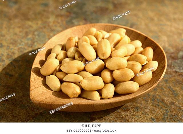Roasted peeled unsalted peanuts on small bamboo plate, photographed on slate with natural light (Selective Focus, Focus one third into the peanuts)