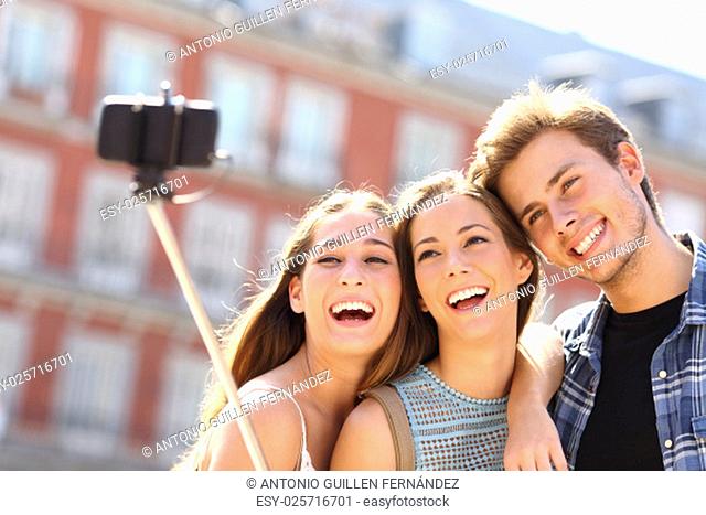 Group of three tourist friends taking selfie with smart phone hand hold monopod in the street