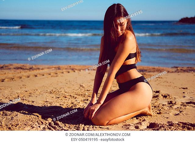 Beautiful brunette woman wearing swimsuit posing on the beach near the sea