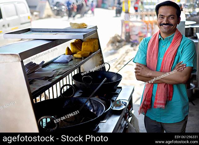 Happy street food vendor posing in front of camera with arms folded