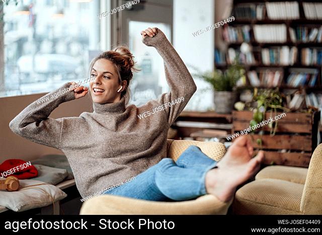Smiling mid adult woman sitting with hand raised at cafe