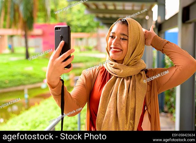 Portrait of young beautiful Indian Muslim woman with hijab relaxing at the park outdoors
