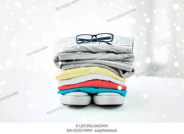 clothes, personal staff and objects concept - close up of folded shirts, pants, glasses and shoes on table at home over snow effect