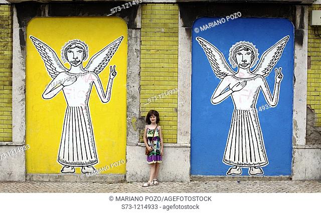 Girl near a wall painting with angels in Lisbon streets, Portugal, Europe