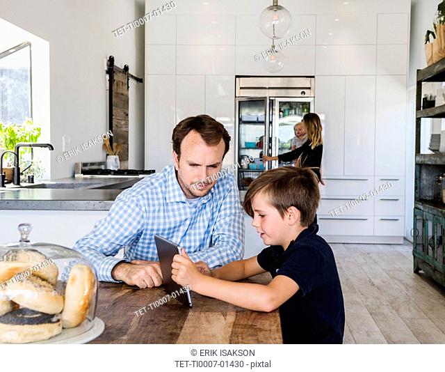 Father and son using digital tablet at dining table