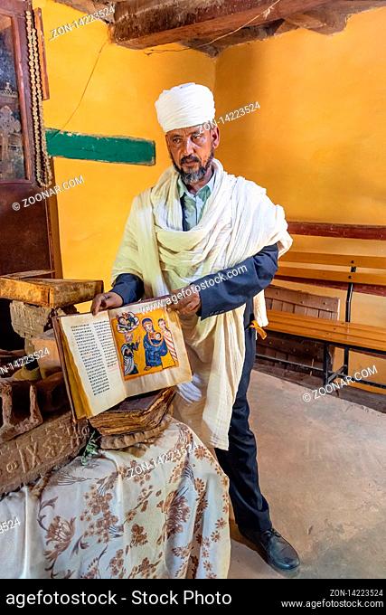 Yeha, Tigray Region, Ethiopia - April 28, 2019: an orthodox priest shows a painted holy bible from the 14th century in Great Temple of the Moon
