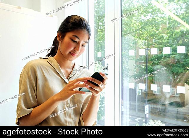 Xoung woman standing at the window reading text messages on her smartphone