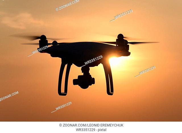 Quadrocopters silhouette against the background of the sunset. Flying drones in the evening sky