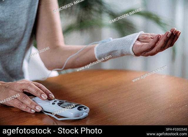 Senior woman doing wrist joint physical therapy with conductive TENS (transcutaneous electrical nerve stimulation) electrode cuff