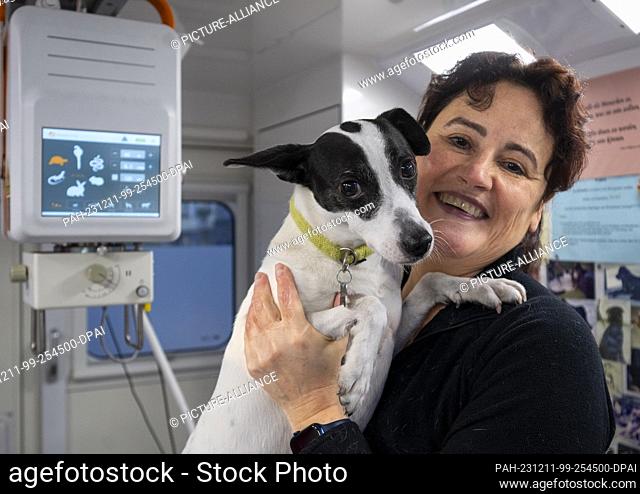 PRODUCTION - 24 November 2023, Berlin: Vet Jeanette Klemmt stands in her mobile veterinary practice during a consultation and holds her dog Amanda in her arms