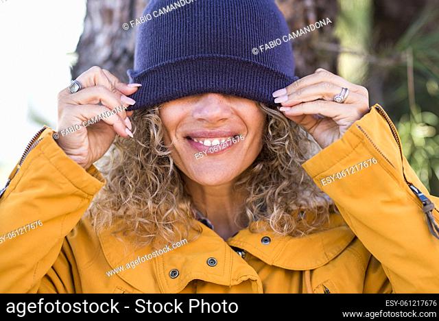 Cheerful adult beautiful woman portrait covering his eyes with winter cup - happy people enjoy outdoor leisure activity - pretty smile and teeth concept -...