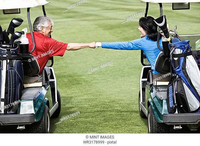 A senior couple doing a fist bump between golf carts on the fairway of a golf course