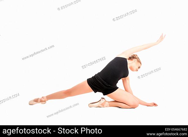 Young blonde girl in black and ballet shoes posing on floor in studio.Isolated