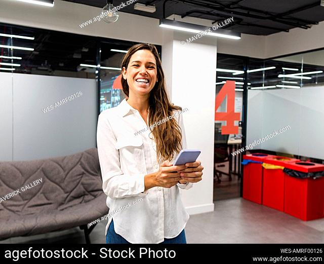 Happy businesswoman with smart phone in office