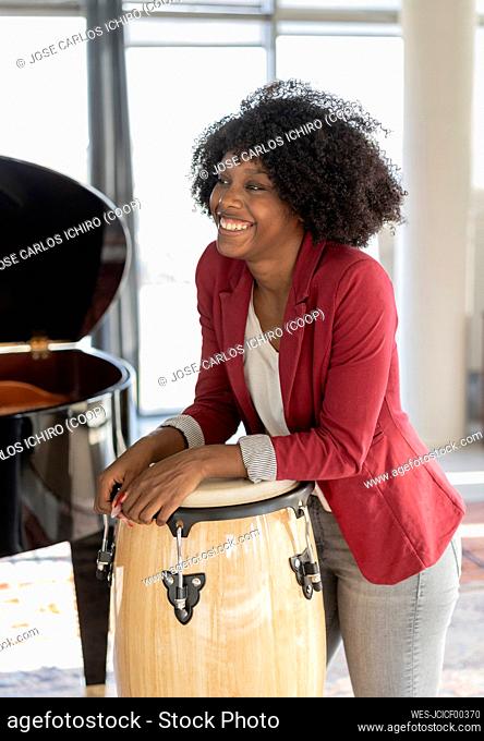Happy businesswoman with Afro hairstyle leaning on conga drum in office