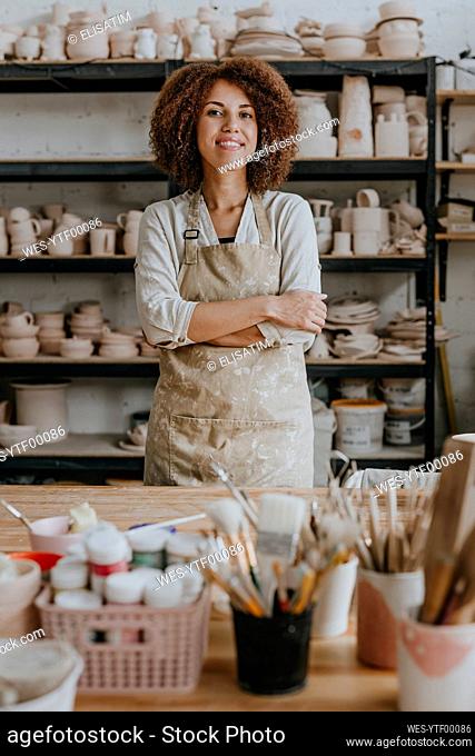 Smiling young craftswoman standing with arms crossed at workshop