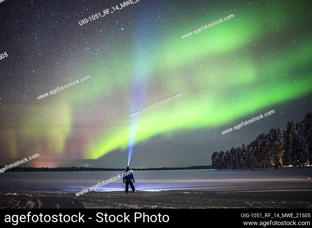 Person under Northern Lights (aurora borealis) display of colourful green and purple in Finnish Lapland, inside Arctic Circle in Finland