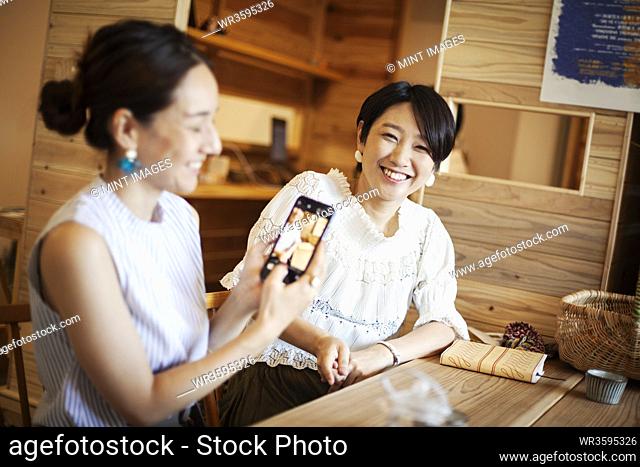 Two Japanese women sitting at a table in a vegetarian cafe, using mobile phone