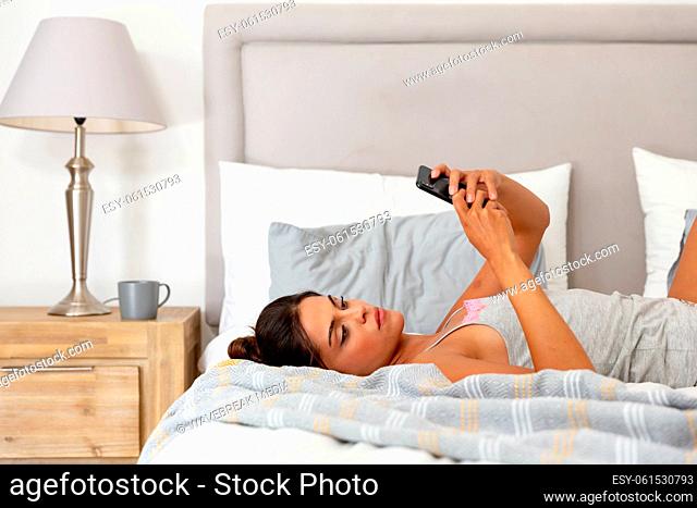 Caucasian woman lying on bed using smartphone and smiling