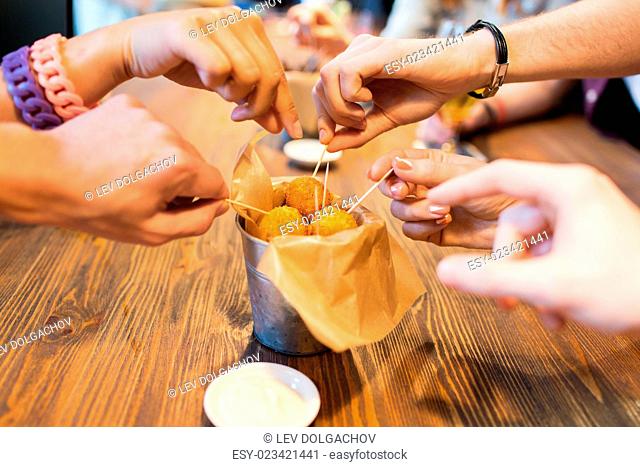 fast food, junk food, unhealthy eating and culinary concept - close up of people hands taking cheese balls with skewers at bar or restaurant