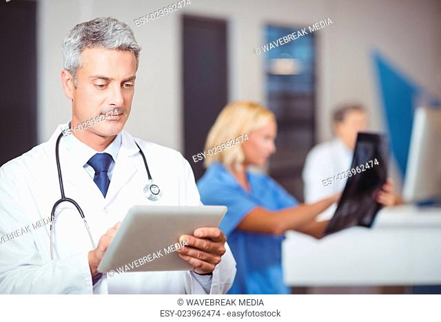 Male doctor using digital tablet with colleague checking X-ray