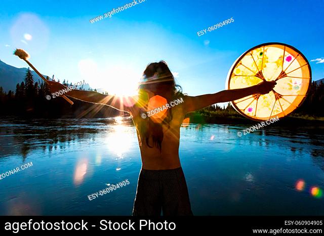 A close up and rear view with lens flare of a man seeking divination, embracing nature with open arms during a spiritual vacation with sacred drum